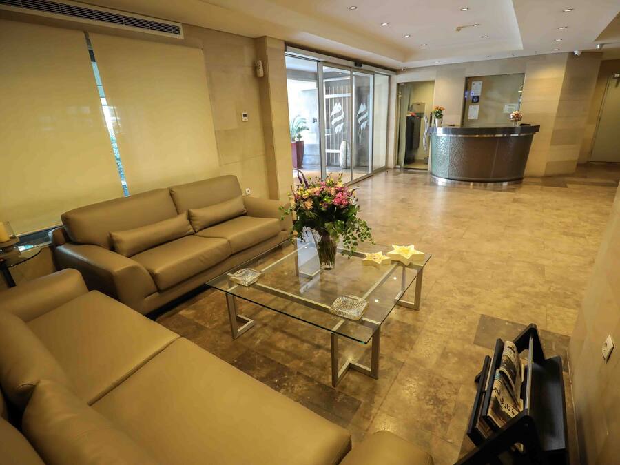 Un hall d’hôtel moderne avec un comptoir d’accueil, une table basse en verre agrémentée d’objets décoratifs et un canapé beige.