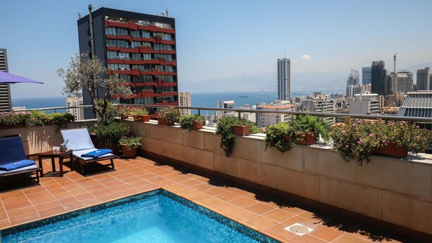 A rooftop pool area with lounge chairs and potted plants, overlooking a cityscape and the sea. - Sky Suites (Beirut)