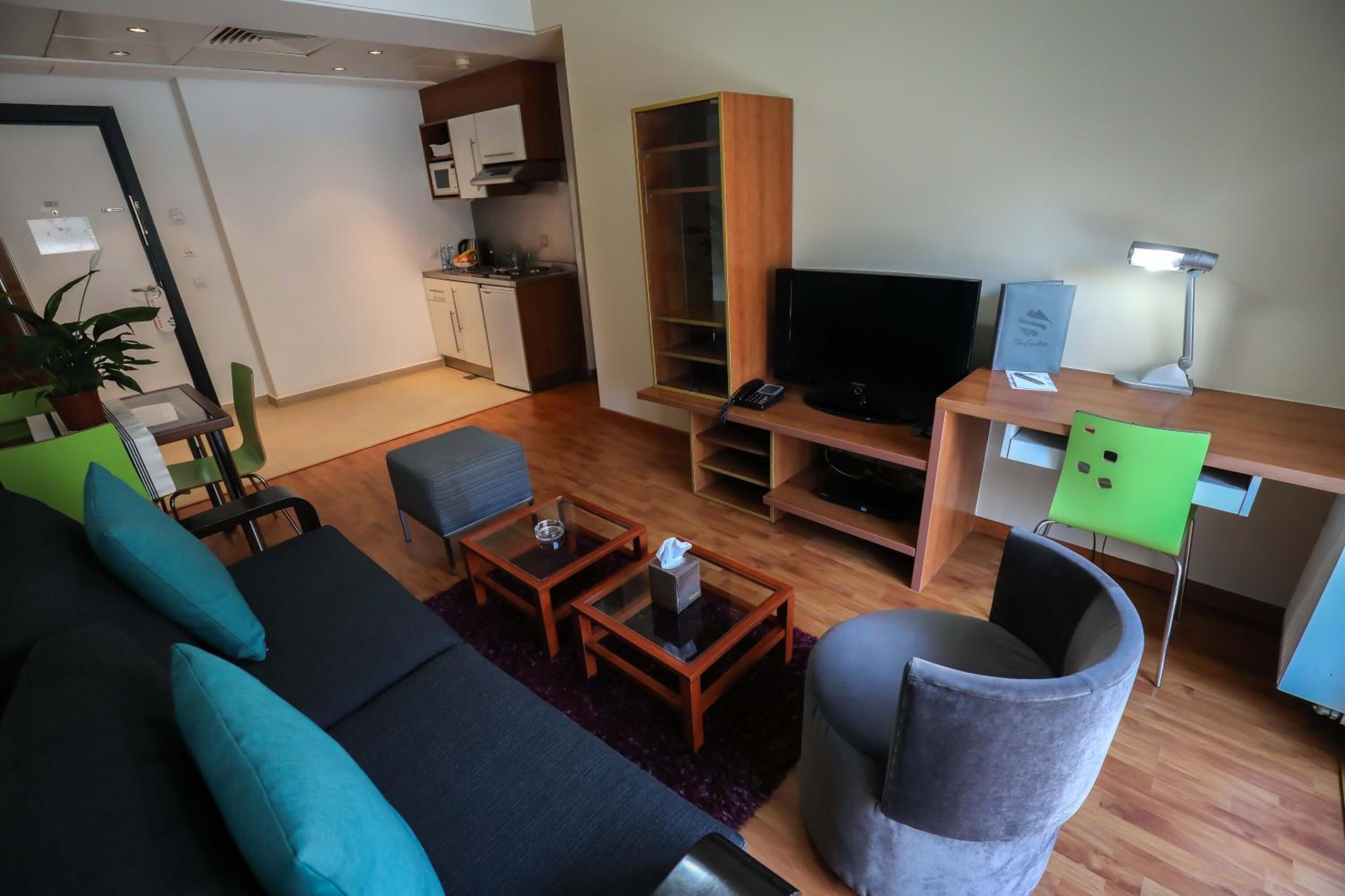 Una sala de estar moderna con un sofá, una mesa de centro y un televisor. Hay una zona de cocina con armarios y un microondas.
