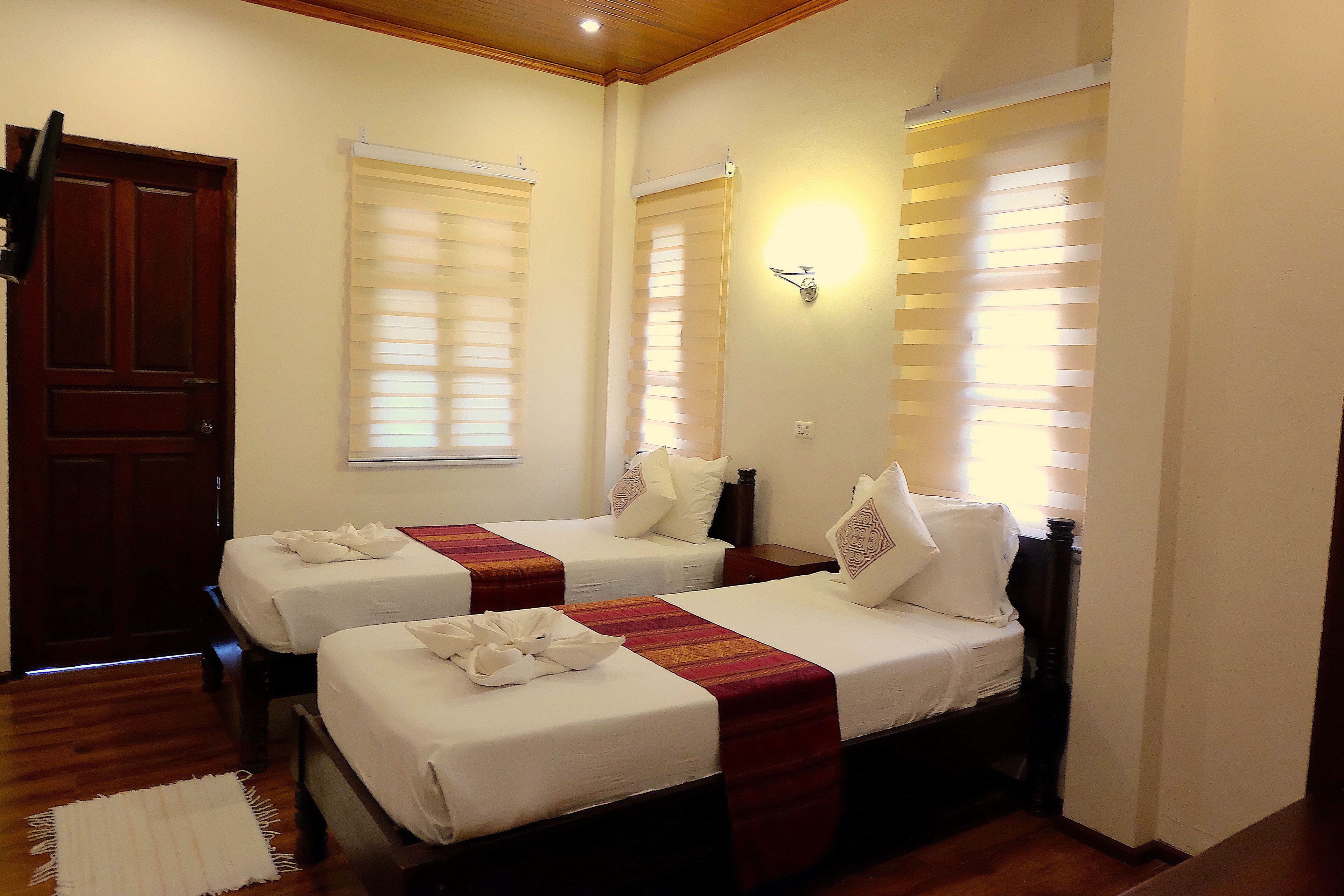 Quarto de hotel com duas camas de solteiro, piso de madeira, porta de madeira e parede branca.