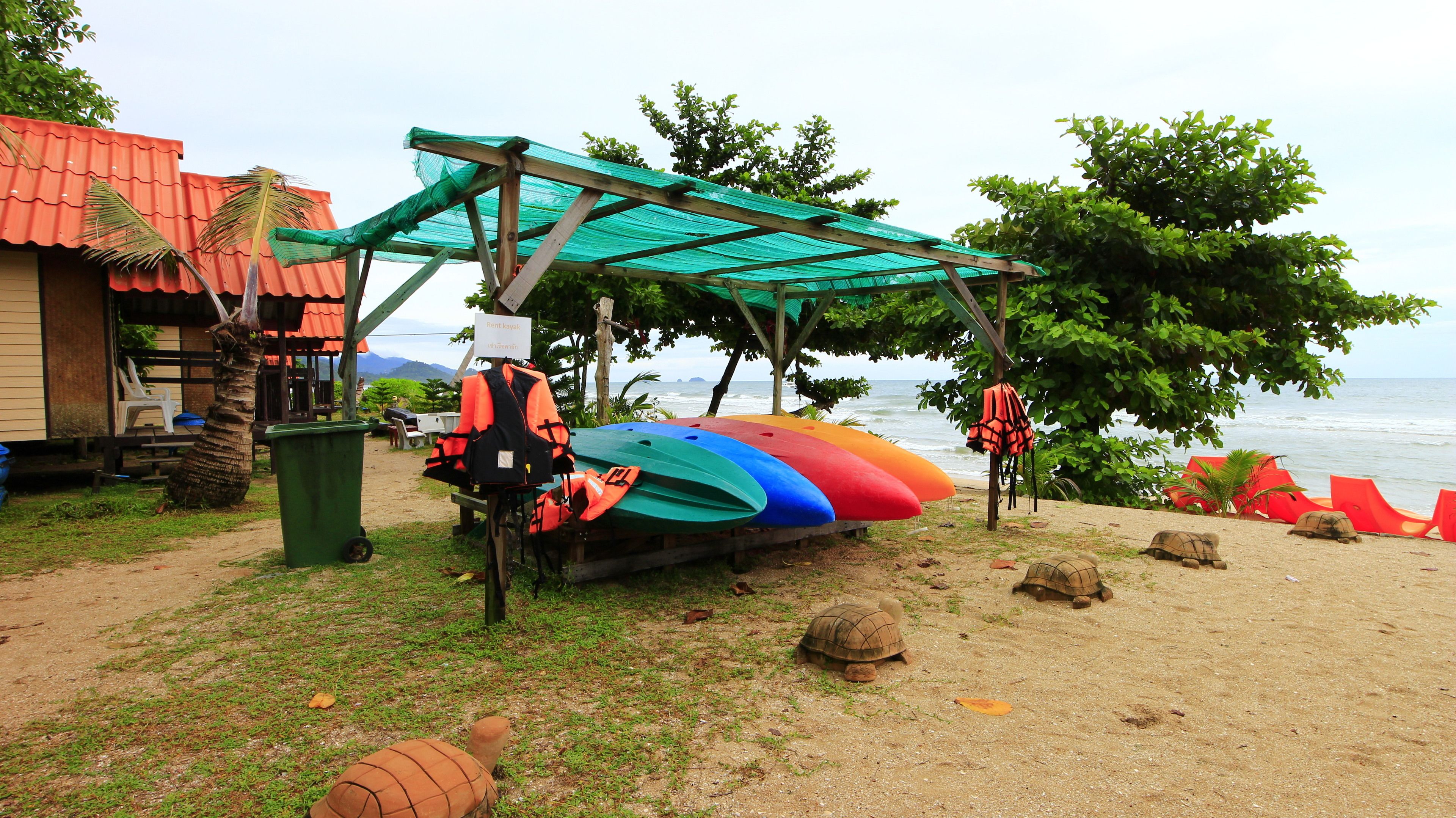A beachside area with colorful kayaks, a wooden structure, and a sign indicating a rental service.
