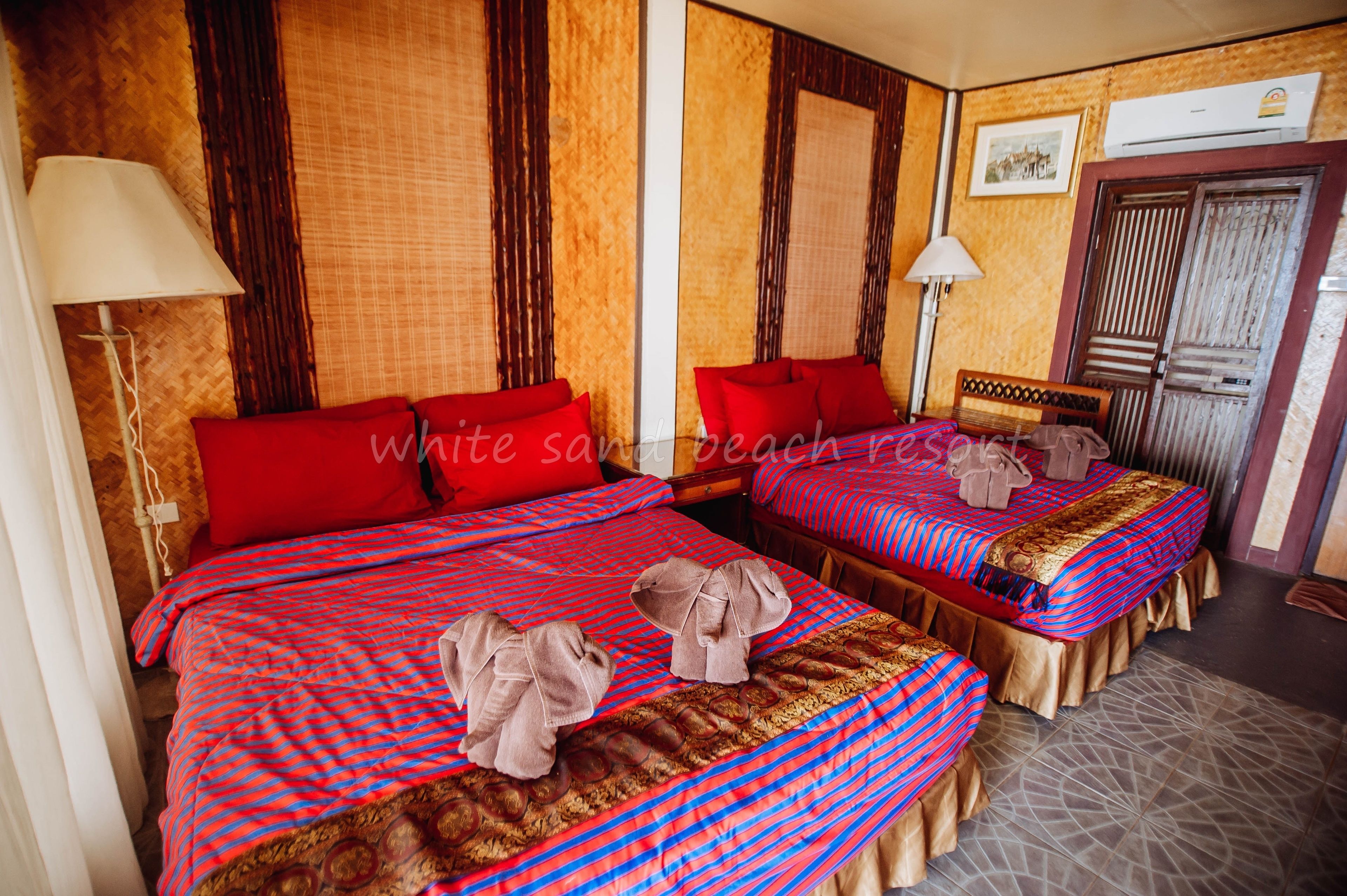 Habitación de hotel con dos camas, ropa de cama roja y cabecera de madera.