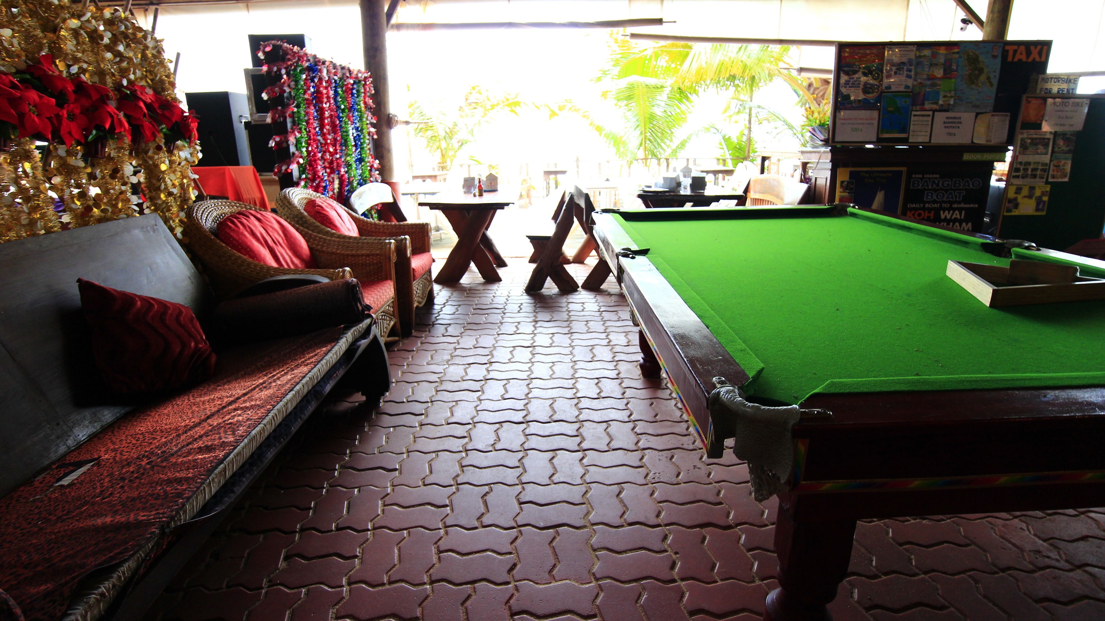 A billiards table, a sofa with red cushions, and a wall decorated with colorful garlands.