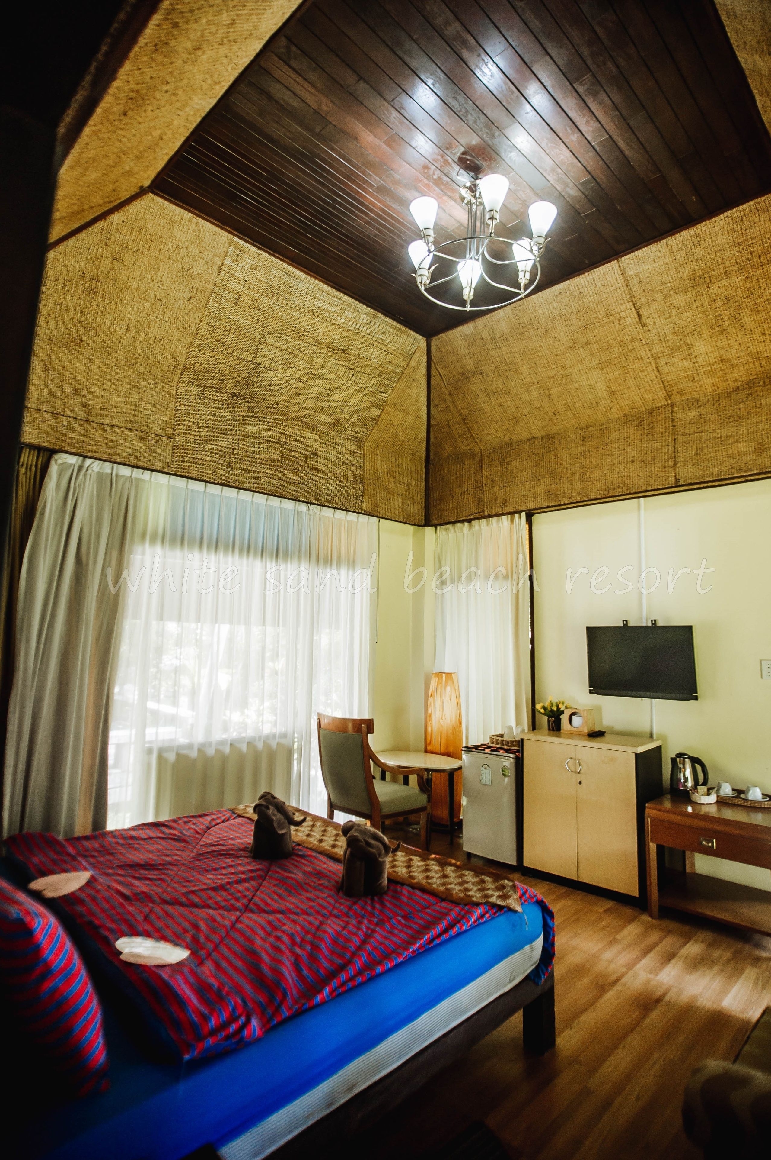 Ein Schlafzimmer mit Bett, Schreibtisch, Sessel, Fernseher und Deckenventilator.