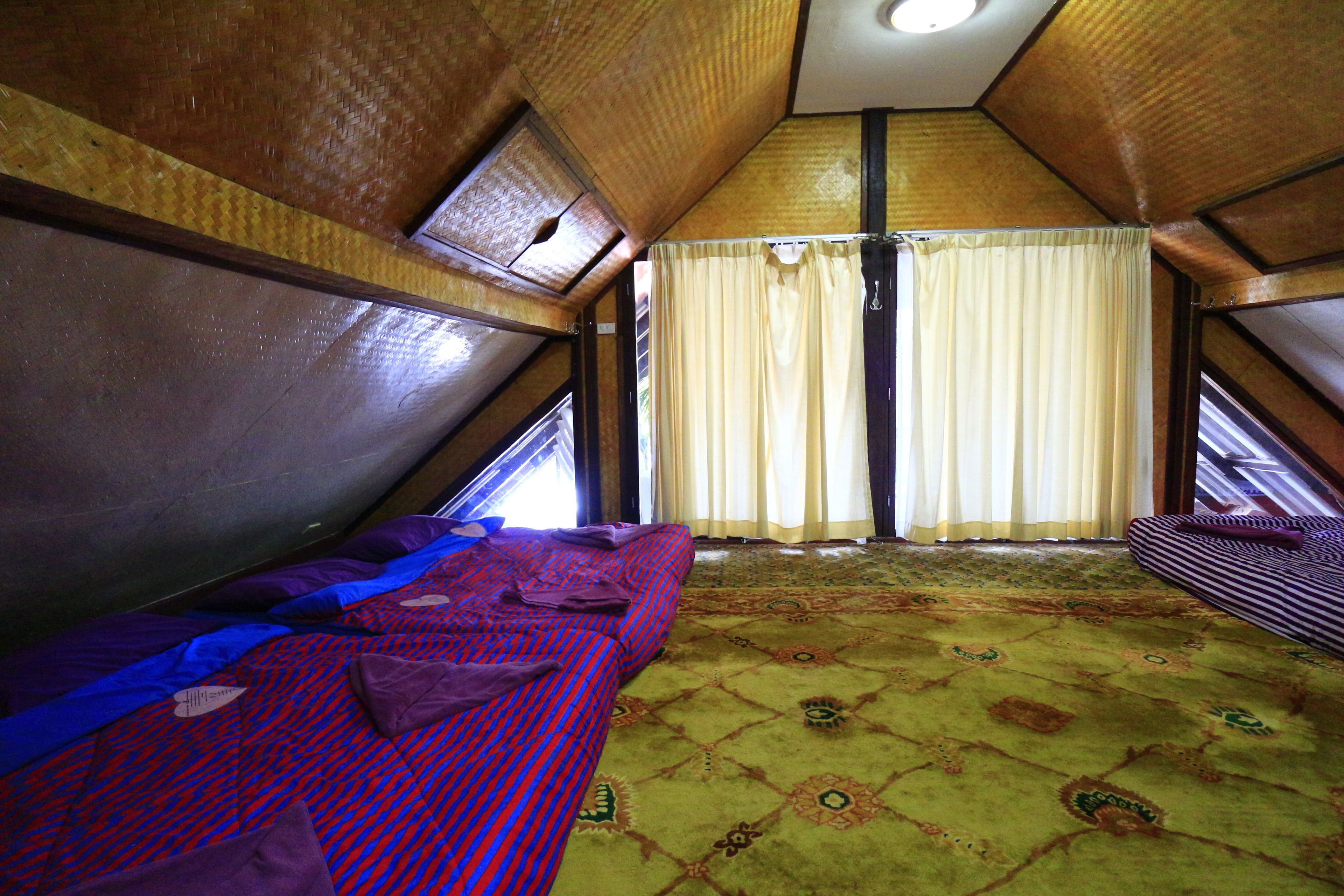 A room with a sloped ceiling, a bed with a patterned bedspread, a window with curtains, and a patterned carpet.