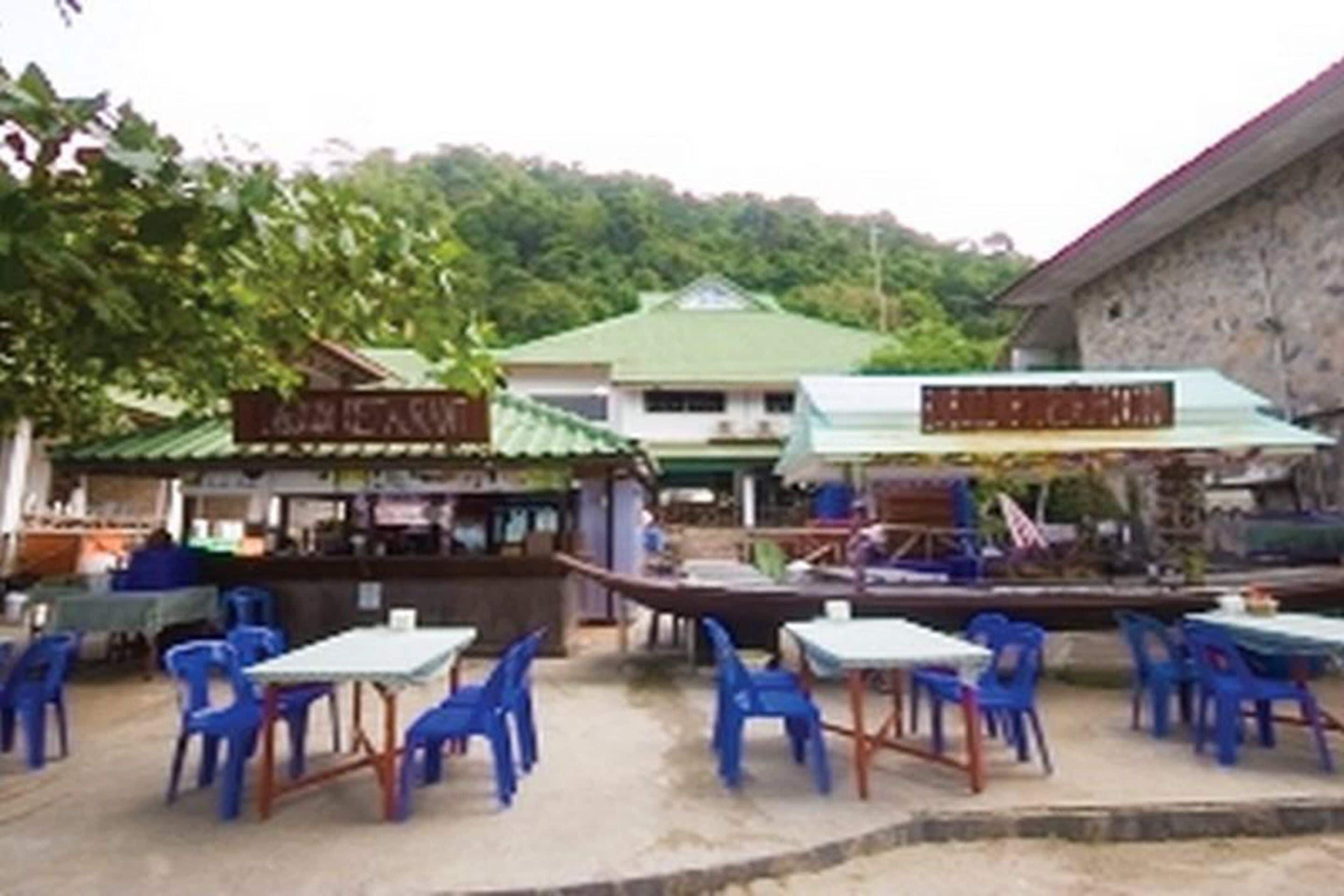 An outdoor dining area with blue plastic chairs and tables, a stone building with a green roof, and a sign that reads "BISTRO".