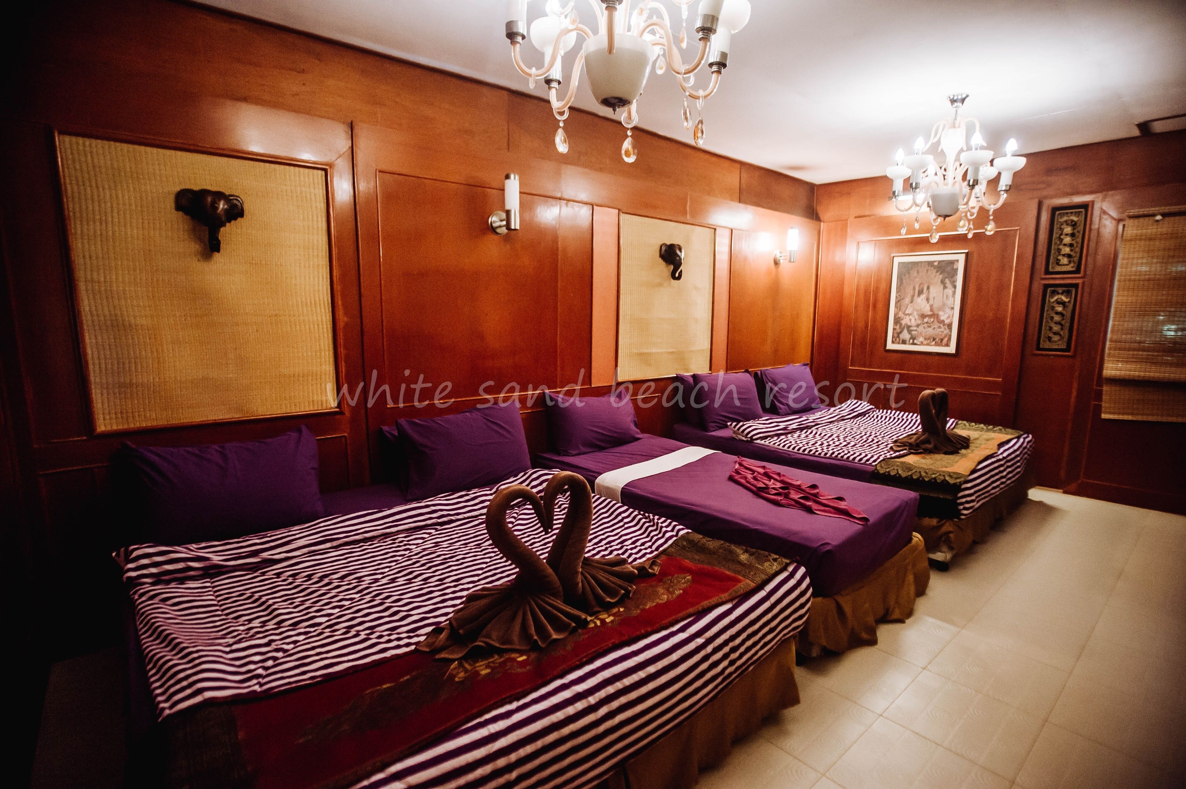 A hotel room with four beds arranged in a row, each with purple bedding and a decorative swan on the bed.