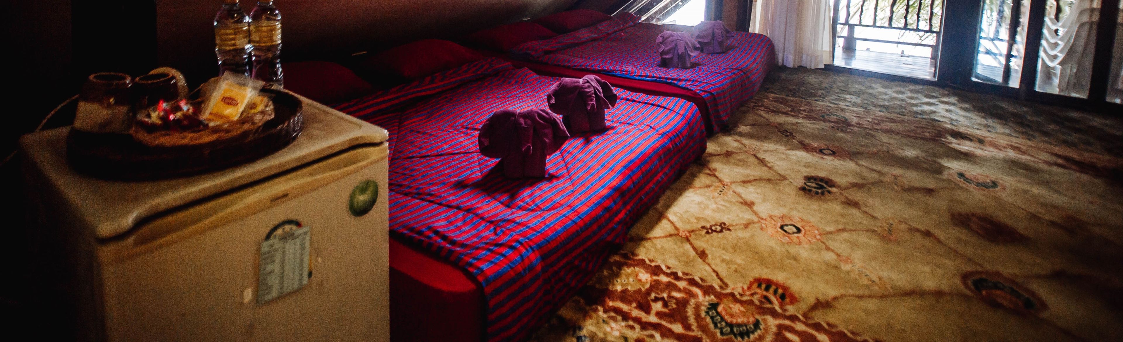 Een kamer met twee bedden, een klein tafeltje met een mand en flessen, en een kamerbreed tapijt met een patroon.