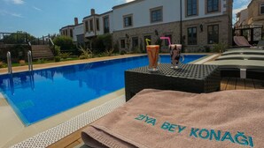 A swimming pool with a clear blue water, a towel with "ZIYA BEY KONAGI" embroidered, and two drinks with straws. - Ziyabey Konagi (Ayvalik)