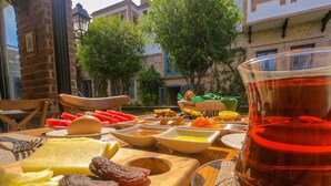 A table with various food items and a glass of red drink, set outdoors with buildings and trees in the background. - Ziyabey Konagi (Ayvalik)