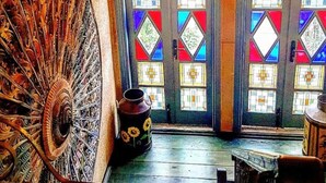 A room with a large, ornate fan, a door with colorful stained glass, and a ceiling light fixture. - Ziyabey Konagi (Ayvalik)