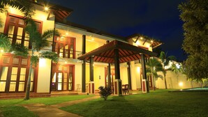 A two-story building with a covered patio area, multiple windows with shutters, and a well-maintained lawn. - Christima Residence (Negombo)