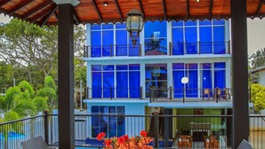 A covered outdoor seating area with wicker furniture and a view of a blue building with balconies. - Christima Residence (Negombo)