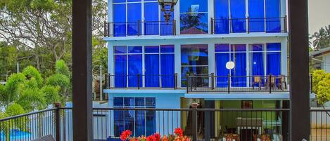 A covered outdoor seating area with wicker furniture and a view of a blue building with balconies.