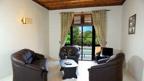 A living room with two brown leather sofas, a small black coffee table with a vase, and a TV stand with a flat-screen TV. - Christima Residence (Negombo)
