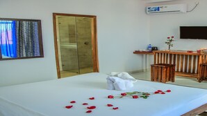 A hotel room with a bed, a wooden side table, a TV mounted on the wall, and a large wooden door. - Christima Residence (Negombo)