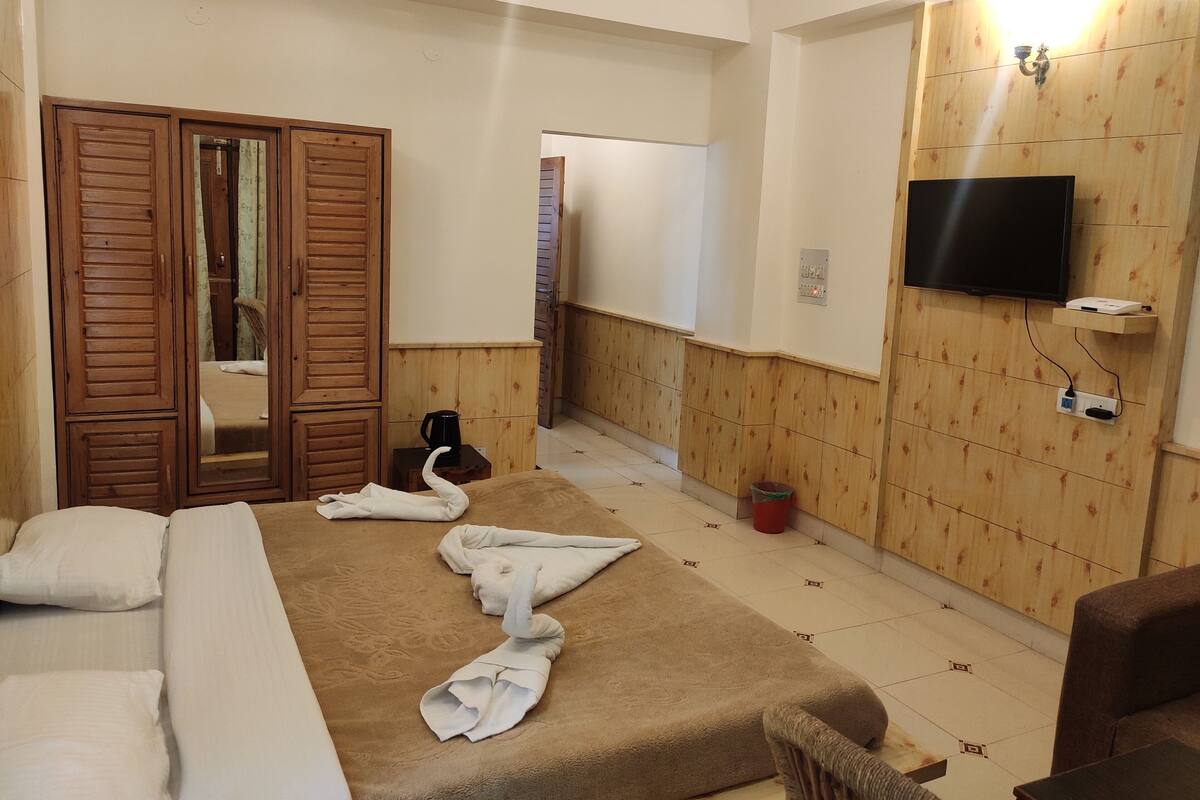 Habitación de hotel con cama, un armario de madera, televisor montado en la pared y una mesita con una taza y un platito.