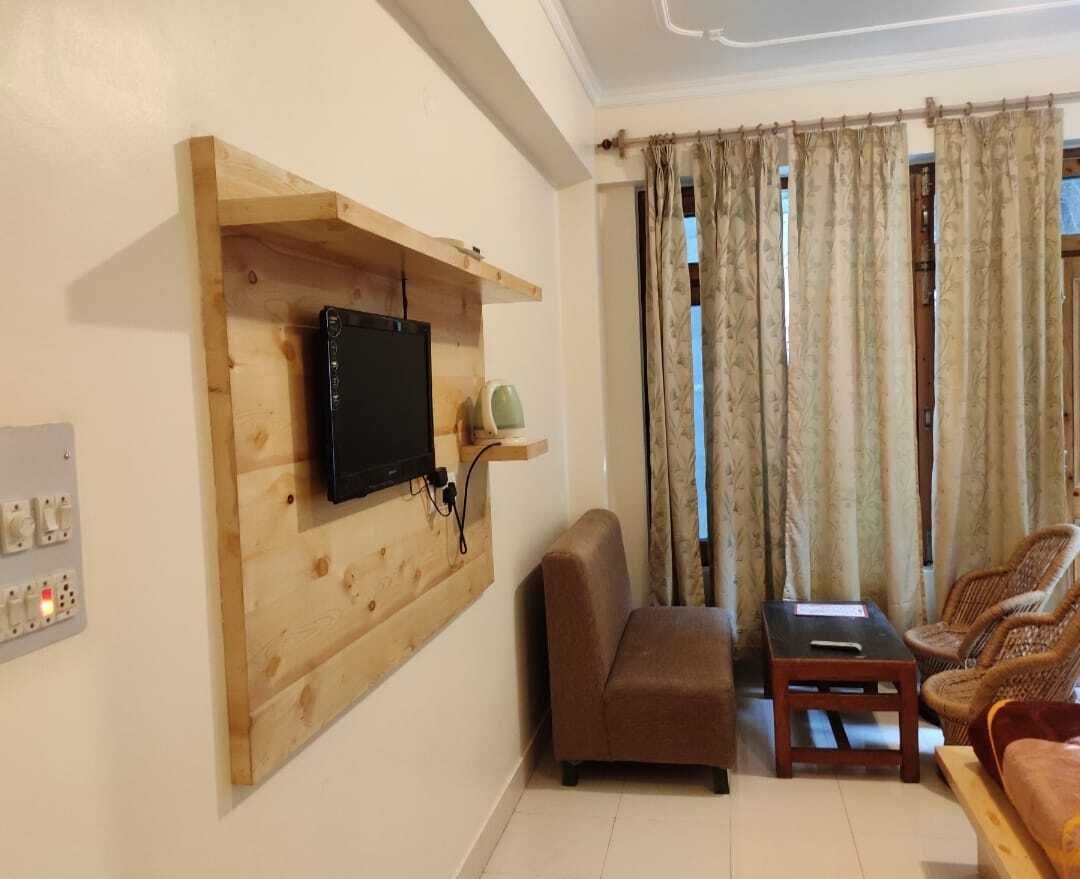 Ein Wohnzimmer mit einer Holz-TV-Konsole, einem braunen Sofa, einem kleinen Tisch und einem Korbstuhl.