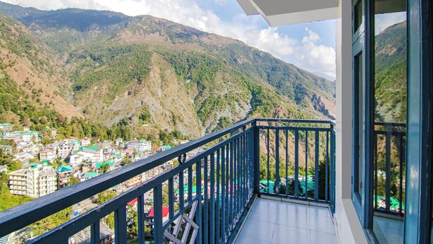 A balcony with a view of a mountainous landscape and a town below. - Greenwoods Inn (Dharamshala)