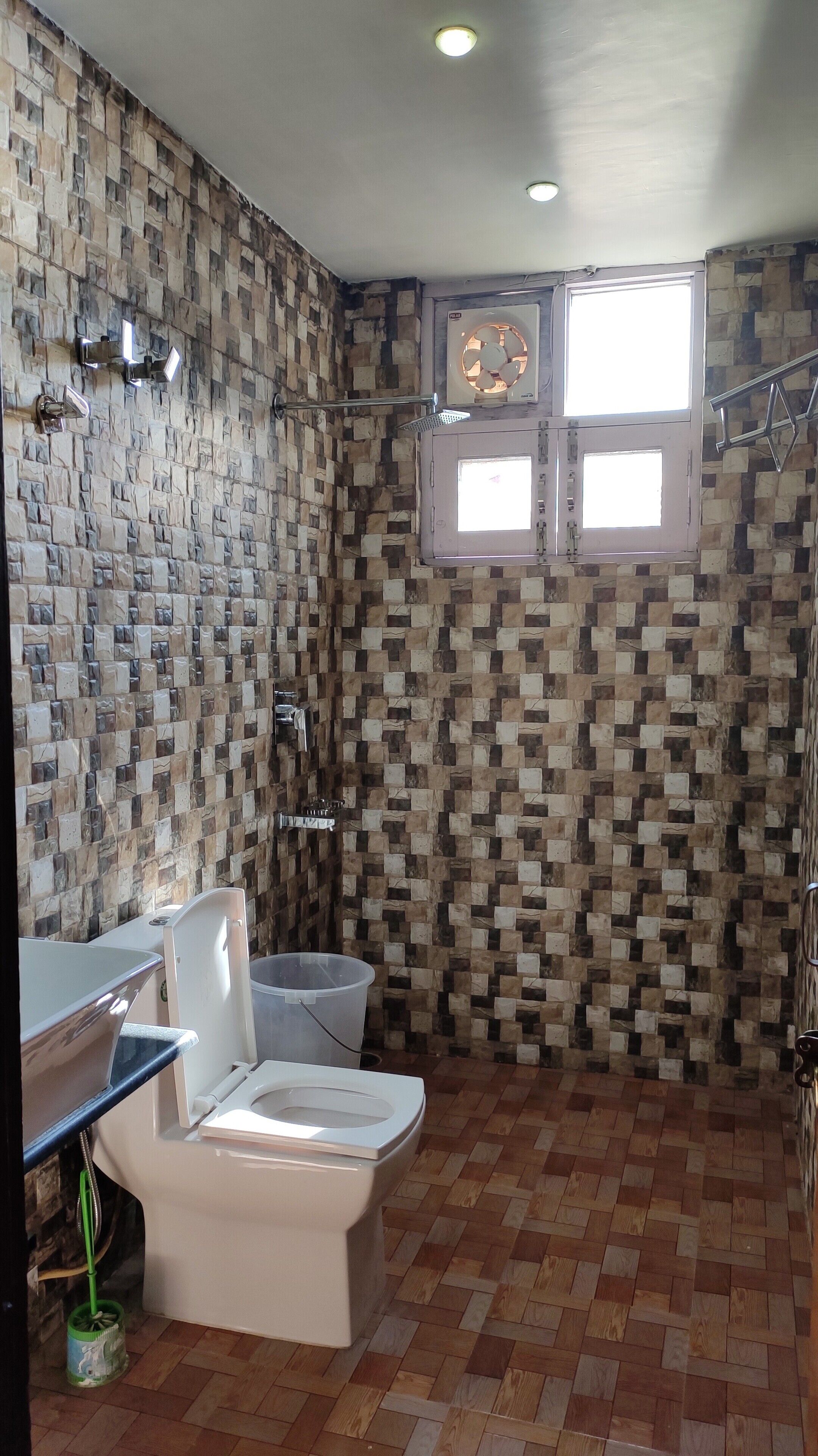 A bathroom with a patterned wall, a toilet, a shower area, and a window.