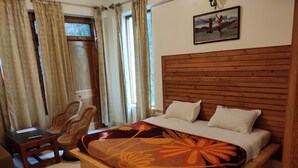 A wooden bed with a floral bedspread, a wooden headboard, a chair, and a small table. - Greenwoods Inn (Dharamshala)