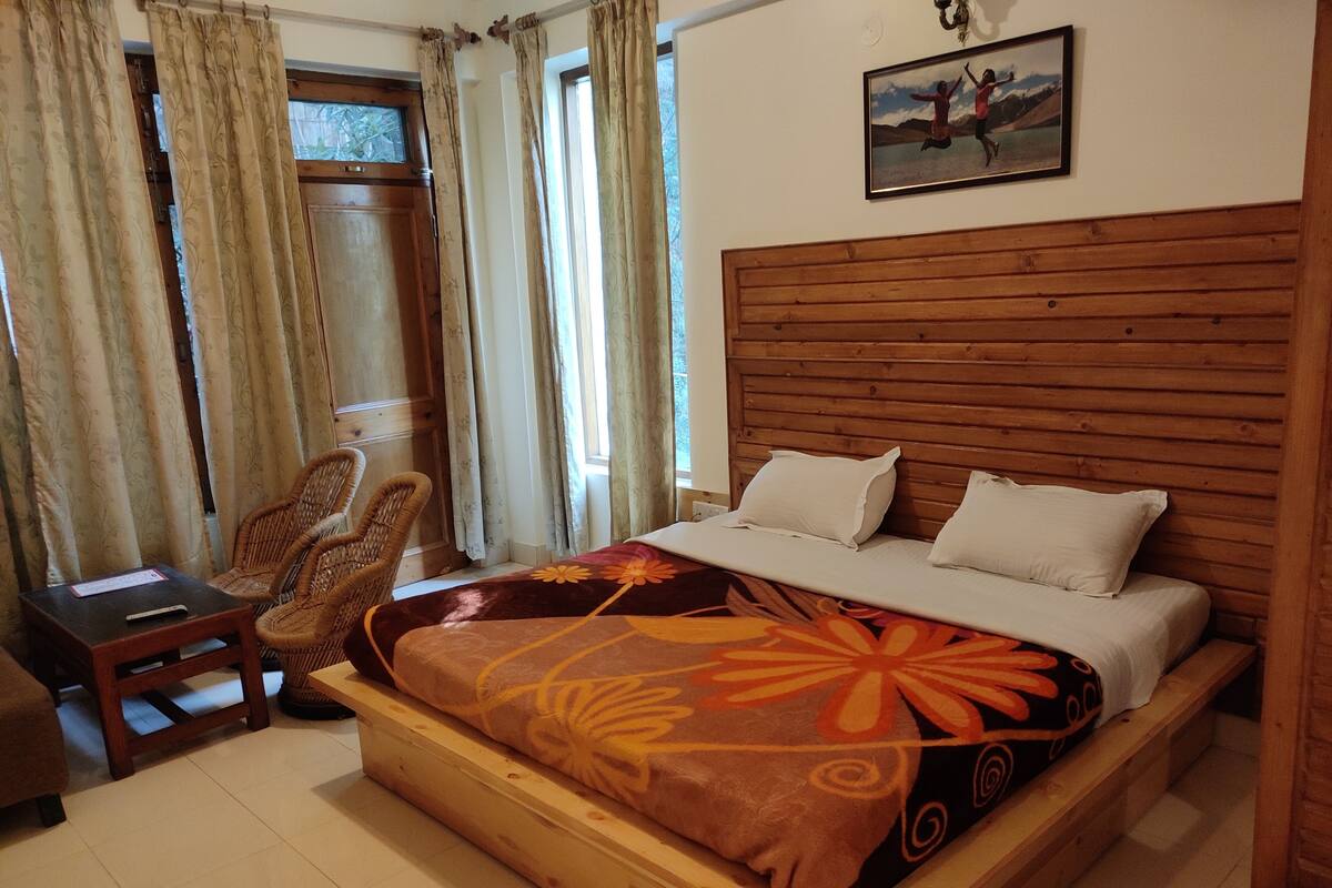 Una cama de madera con una colcha estampada, un cabecero de madera, una silla y una mesita.