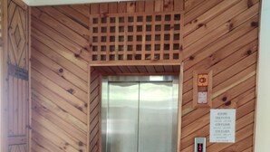 An elevator in a wooden-finished hallway with a sign indicating room numbers on the 3rd, 4th, 5th, and 2nd floors. - Greenwoods Inn (Dharamshala)