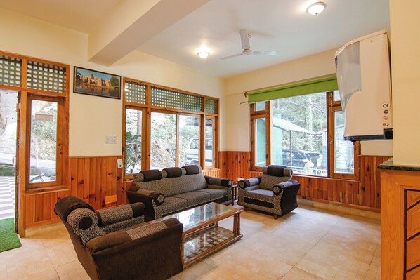 A spacious living room with wooden walls and large windows, furnished with a sofa and chairs.