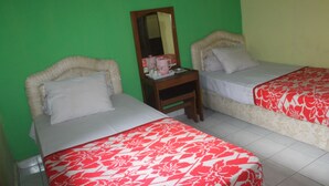 A room with two beds, each with a floral-patterned bedspread, a nightstand with a mirror, and a small table with a pink mug. - Hotel Sakato (Bukittinggi)