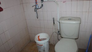 A small bathroom with a toilet, a bucket of paint, and a broom. - Hotel Sakato (Bukittinggi)