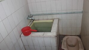 A small bathroom with a toilet, a red bucket, and a bathtub. - Hotel Sakato (Bukittinggi)