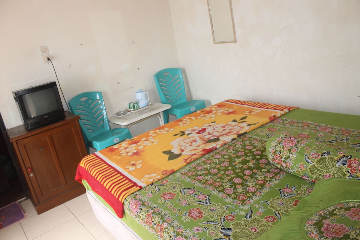 Una habitación con cama, televisión, dos sillas y una mesita.