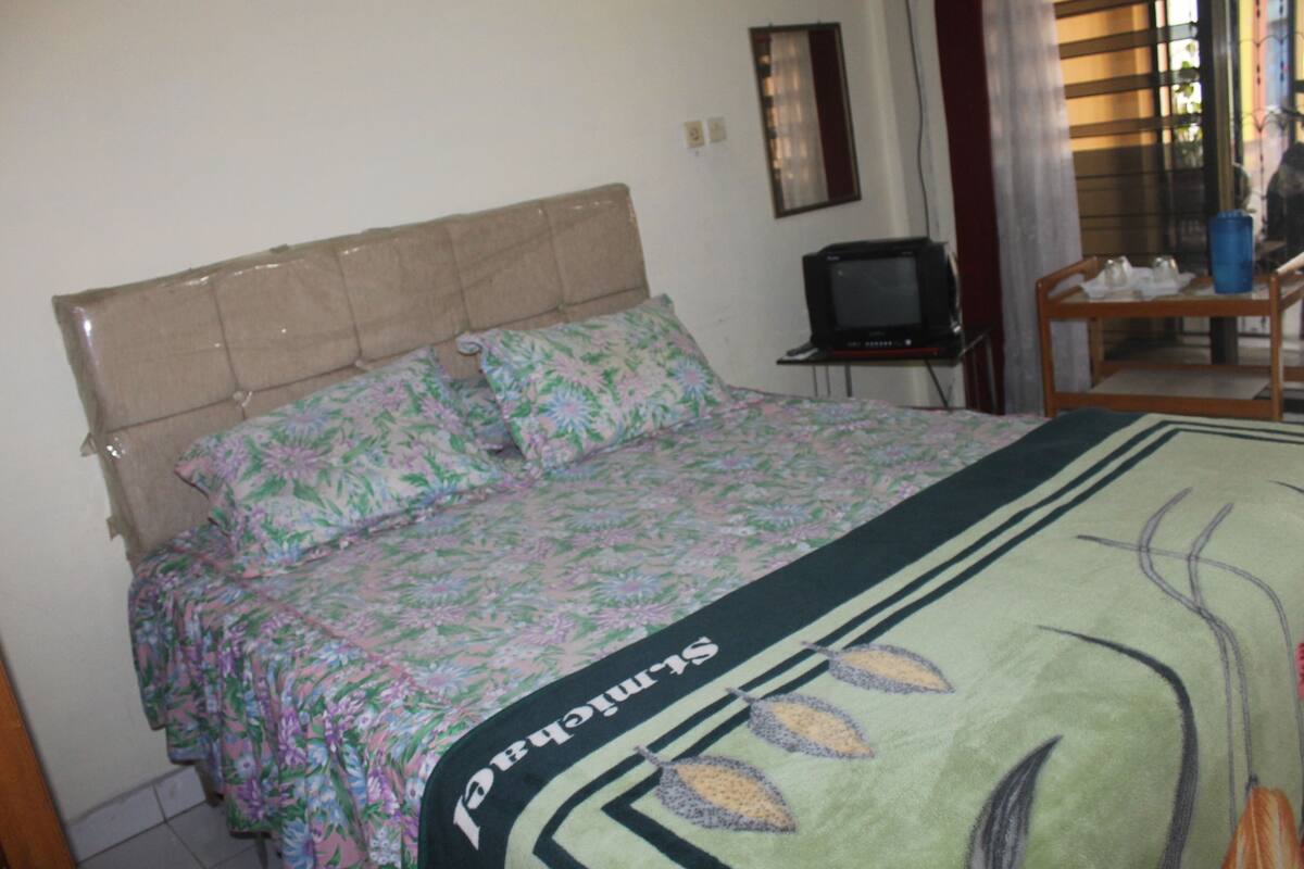 Un dormitorio con una cama, un televisor y una mesita con un jarrón azul.
