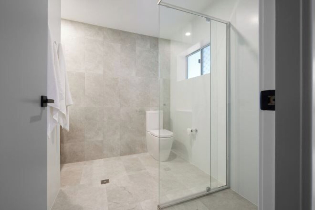 Un baño moderno con cabina de ducha de vidrio, inodoro y una ventana pequeña.