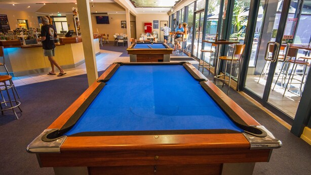 A pool table in a well-lit indoor space with a bar area and seating.