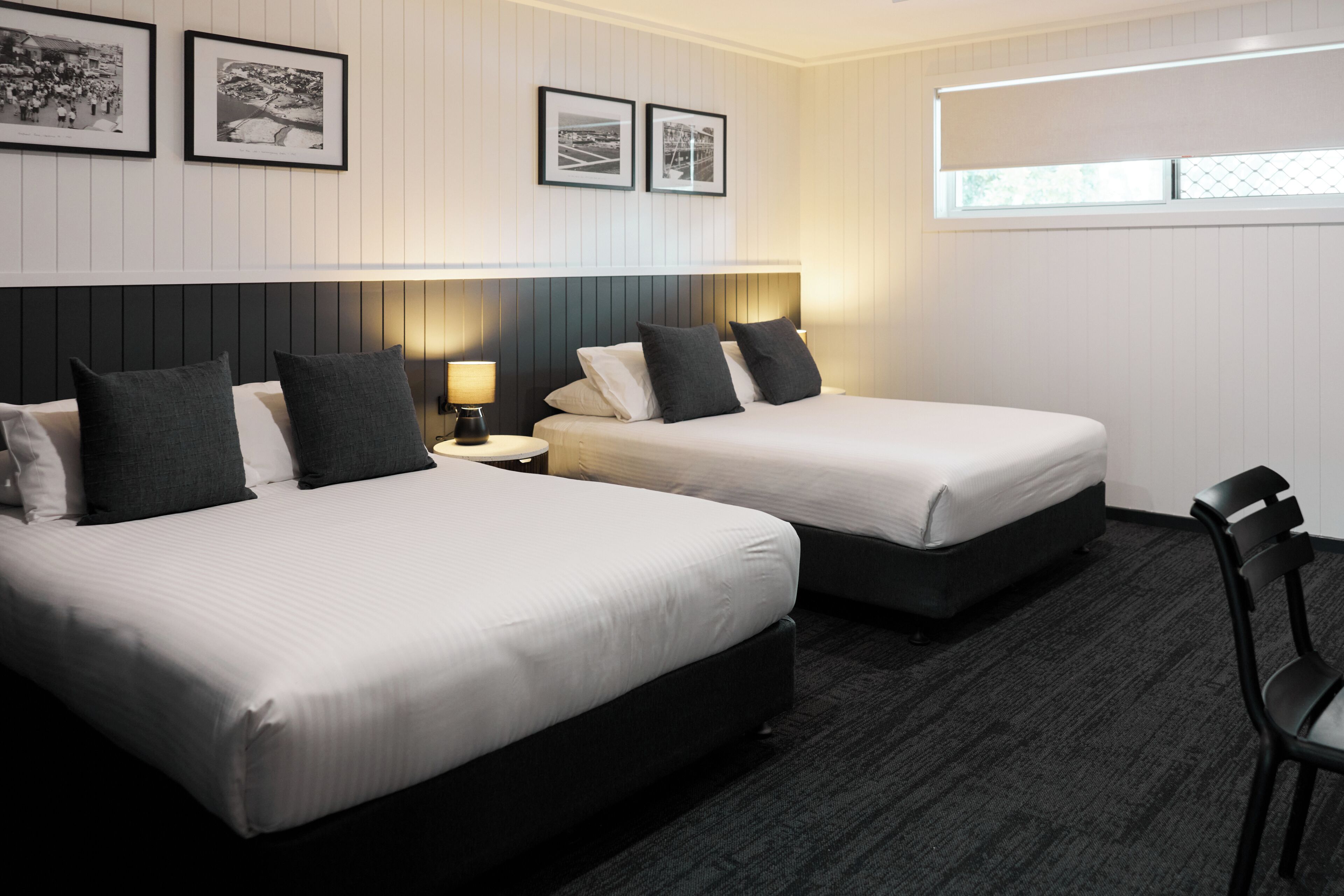 A hotel room with two beds, a nightstand, a chair, and framed pictures on the wall.