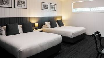 A hotel room with two beds, a nightstand, a chair, and framed pictures on the wall.