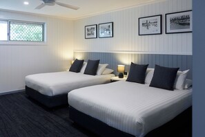 Habitación de hotel con dos camas, ventilador de techo, ventana con vistas y cuadros en la pared.