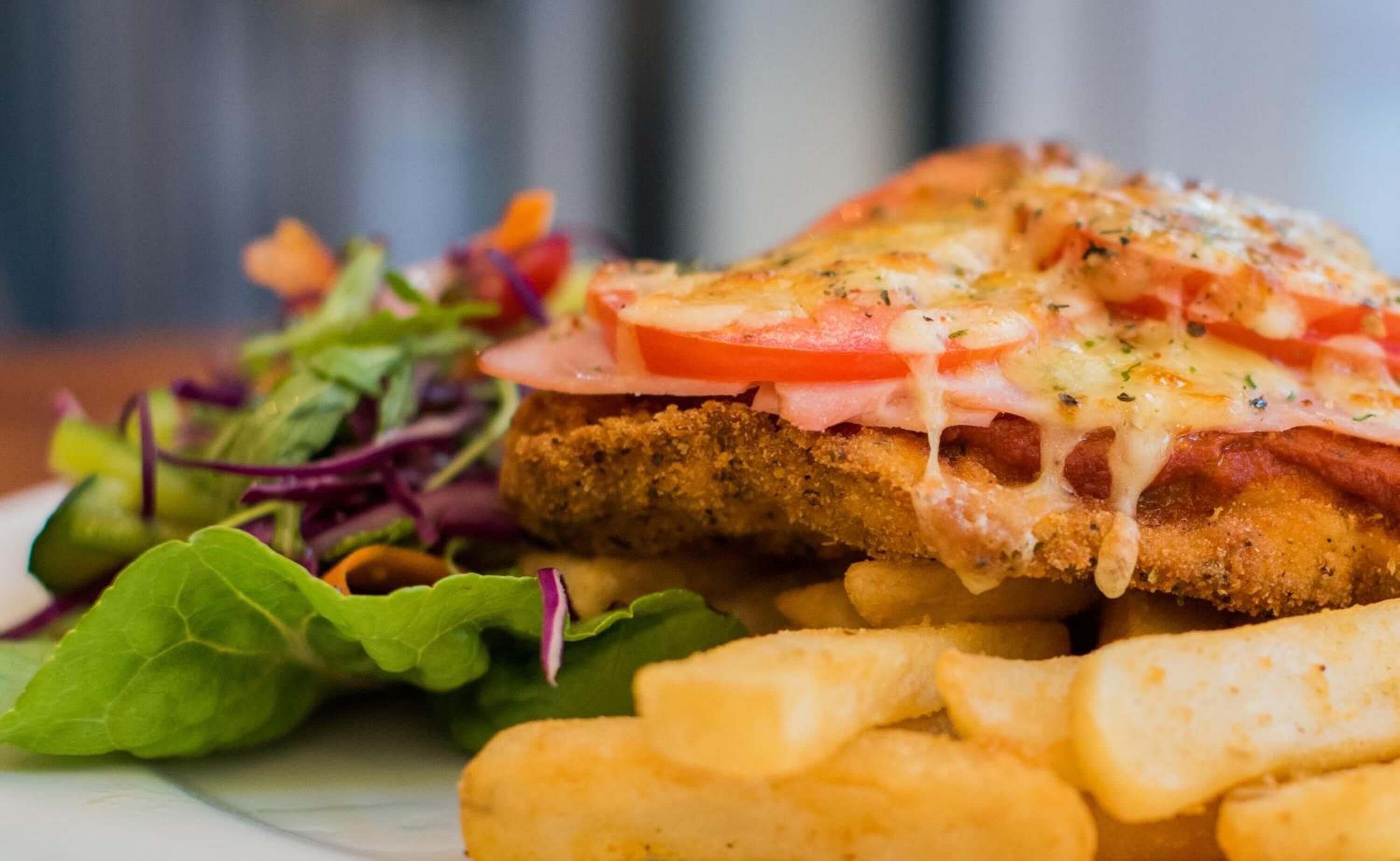 Ein Gericht mit paniertem Schnitzel, Käse und Tomatenscheiben, dazu ein gemischter Salat und Pommes.