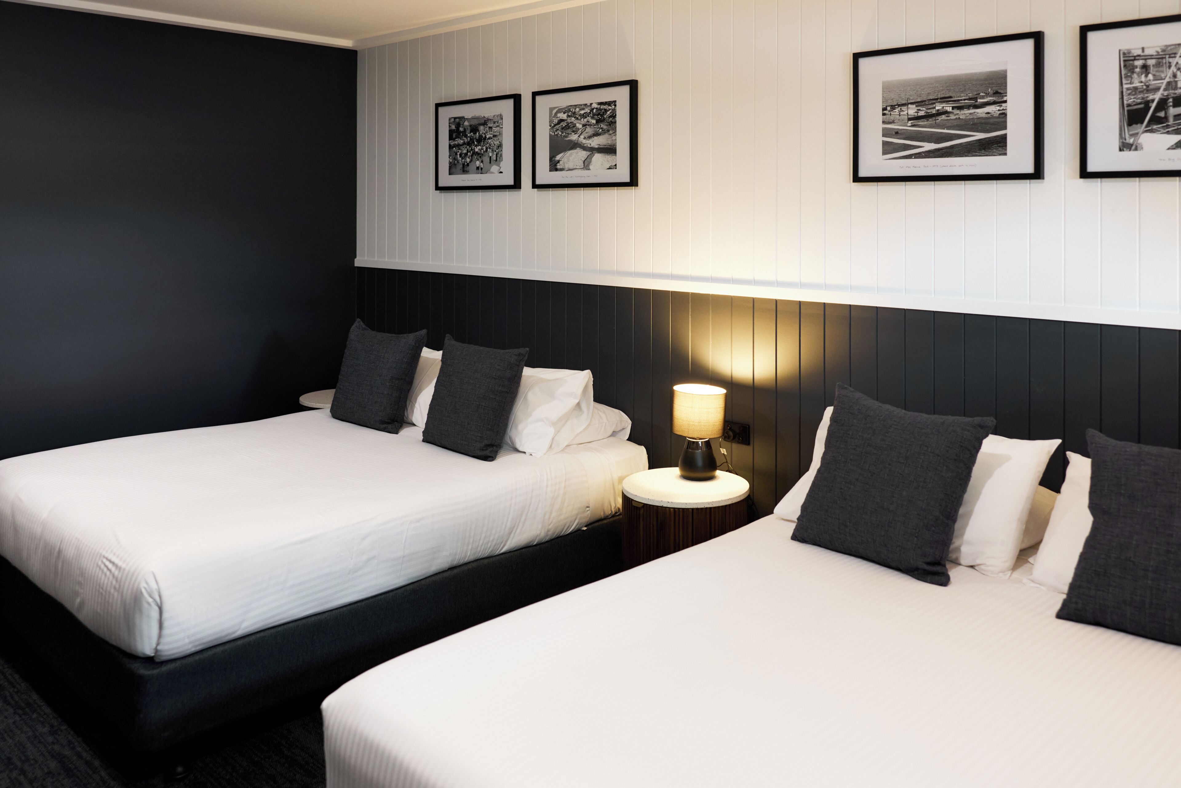 Ein Hotelzimmer mit zwei Betten, einem Nachttisch mit Lampe und gerahmten Bildern an der Wand.
