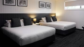 A hotel room with two beds, a nightstand with a lamp, framed pictures on the wall, and a window with blinds.