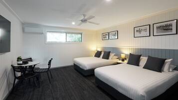 Ein Hotelzimmer mit zwei Betten, einem Schreibtisch mit Stühlen, einem Deckenventilator und gerahmten Bildern an der Wand.