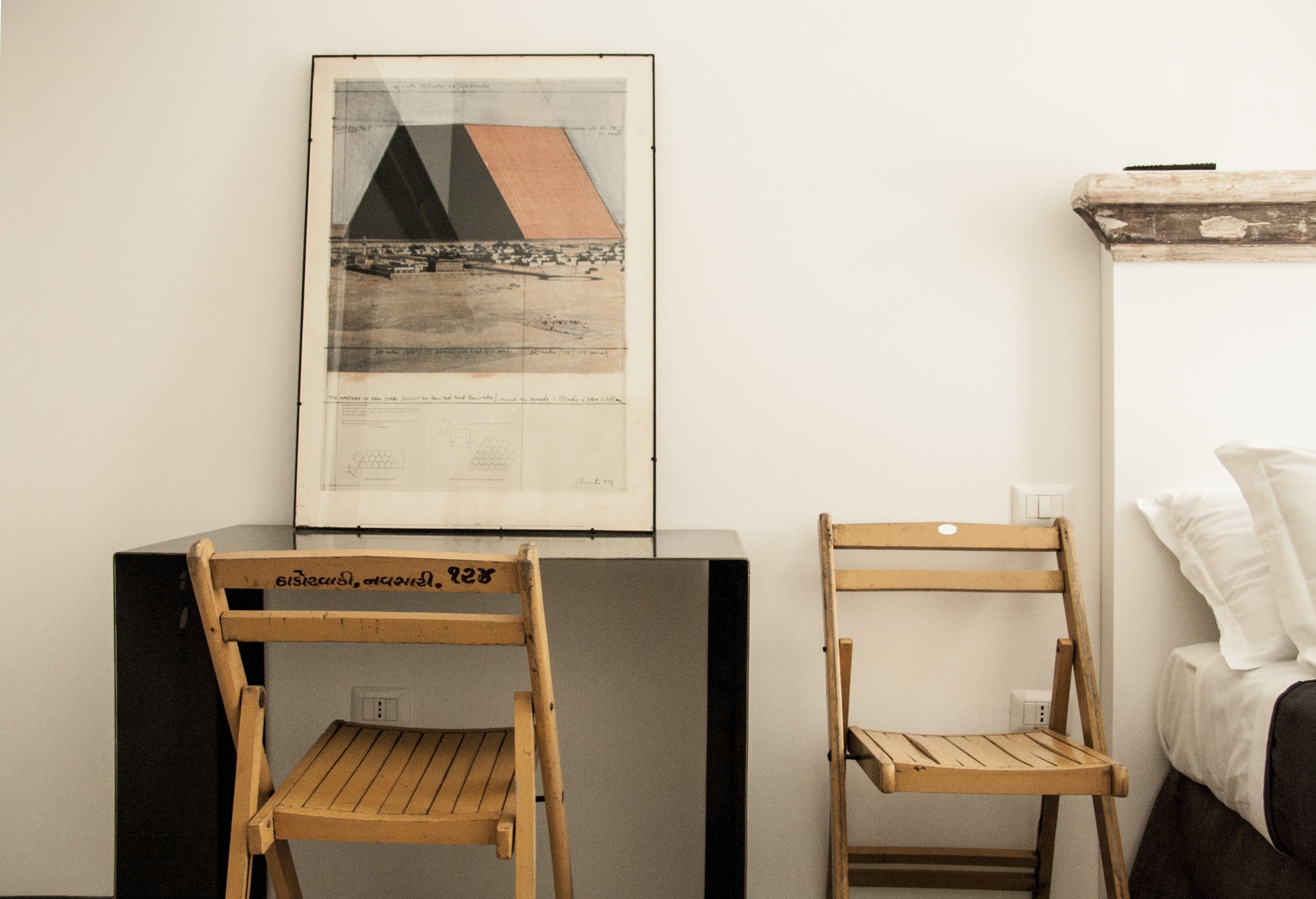 Una habitación con dos sillas de madera, un mapa enmarcado en la pared y una cama con ropa blanca.
