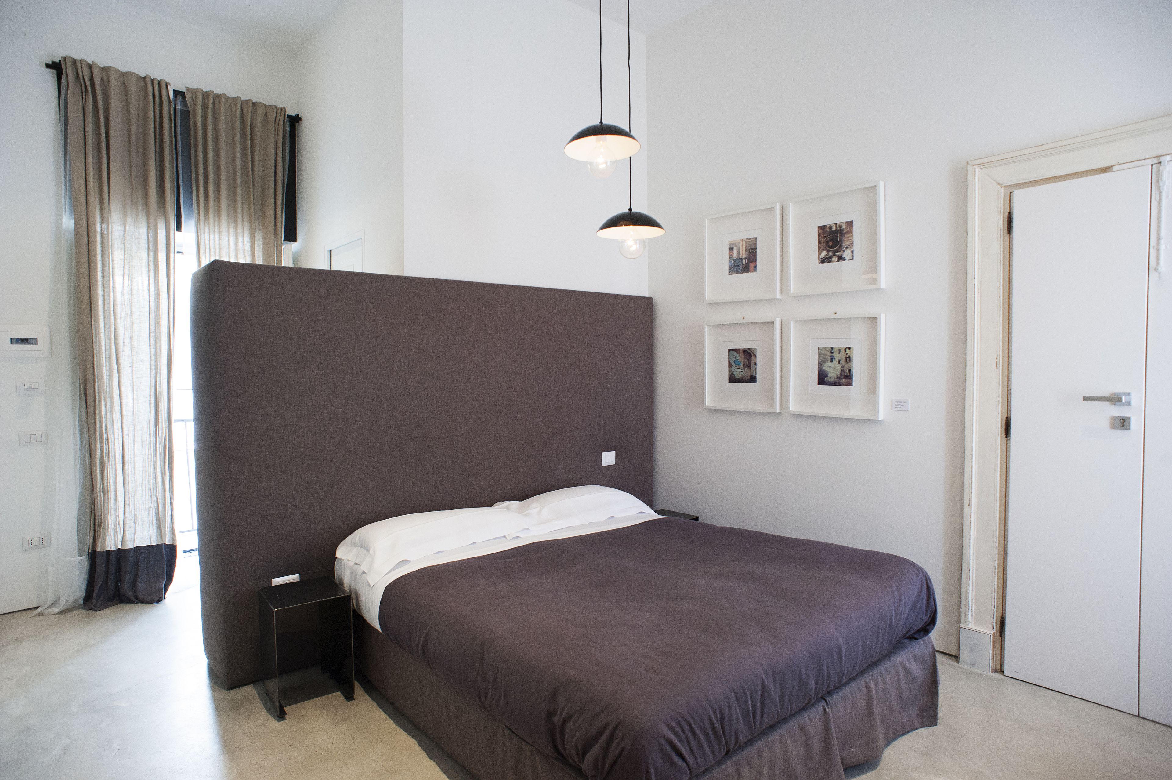 A modern bedroom with a large bed, a bedside table, a wardrobe, and a wall with framed pictures.