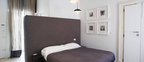 A modern bedroom with a large bed, a bedside table, a wardrobe, and a wall with framed pictures.