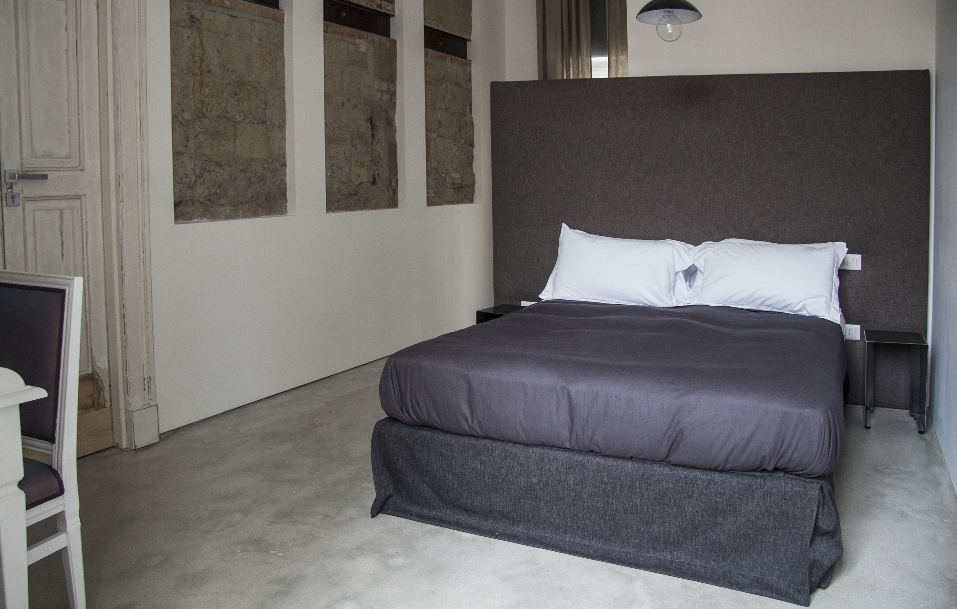 Ein Schlafzimmer mit einem großen Bett, einem Nachttisch, einem Sessel und einer Wandleuchte.