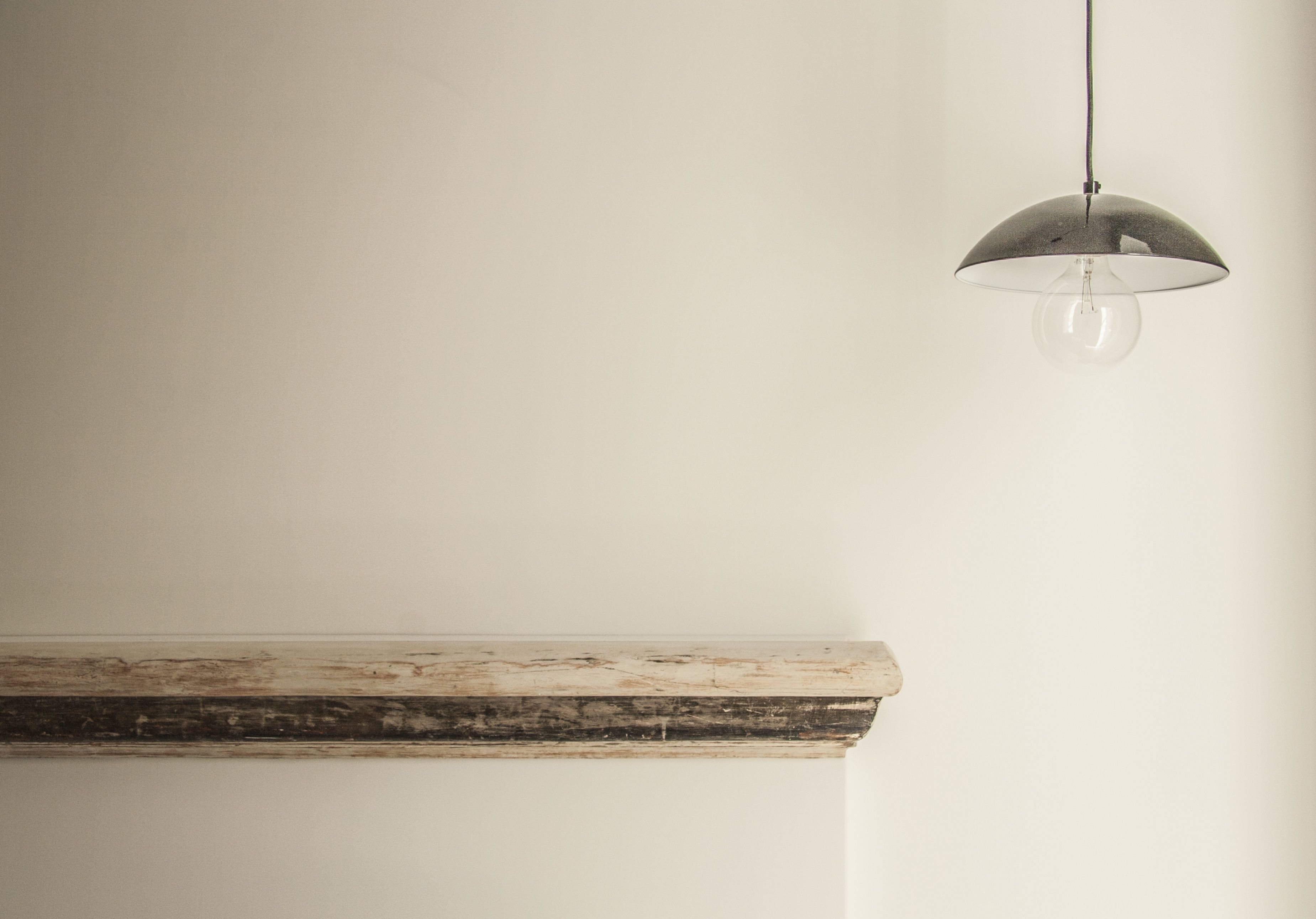 A minimalist room with a wooden mantel and a hanging pendant light.