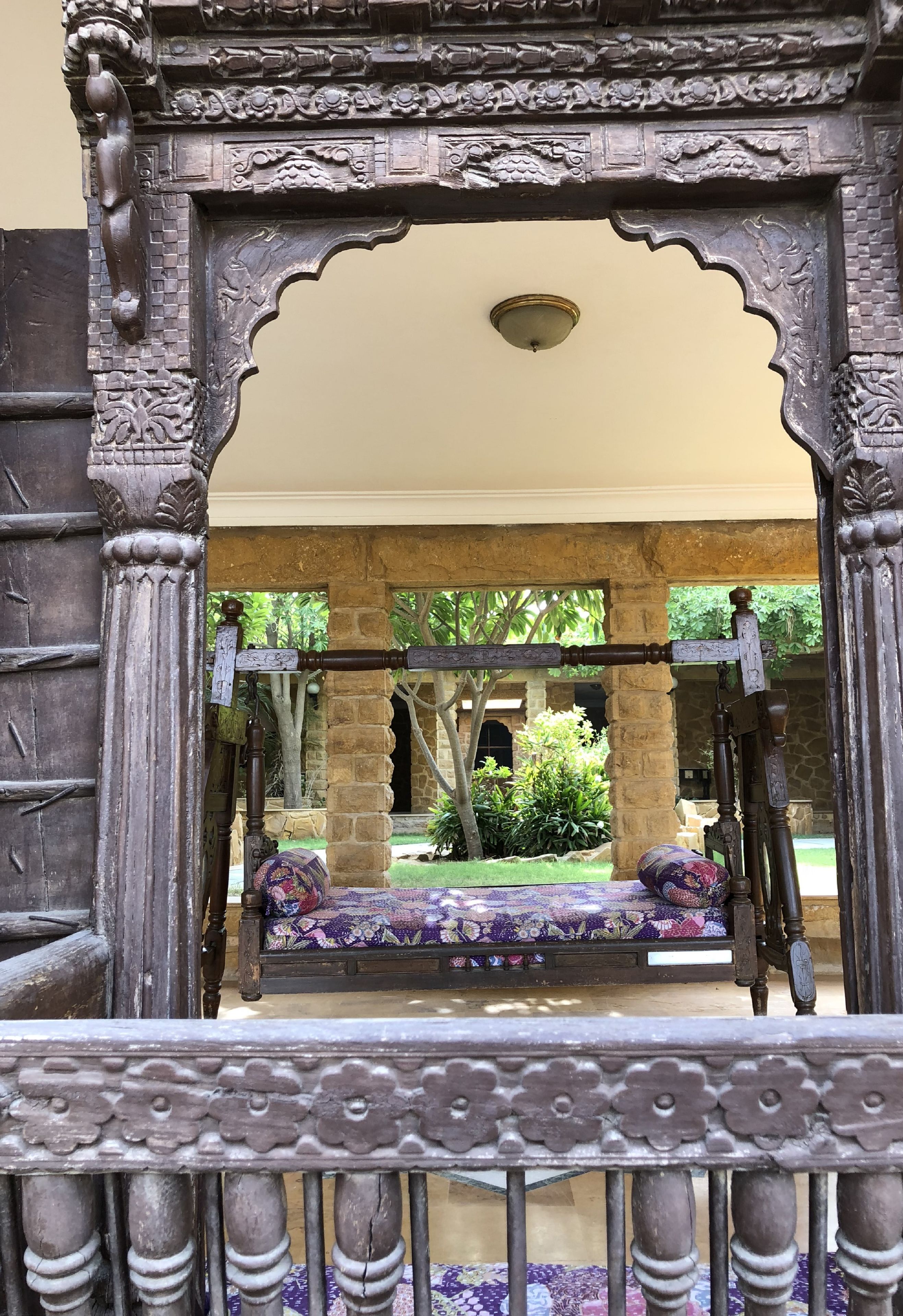 An ornate wrought iron gate with a bench and a swing set in the background.