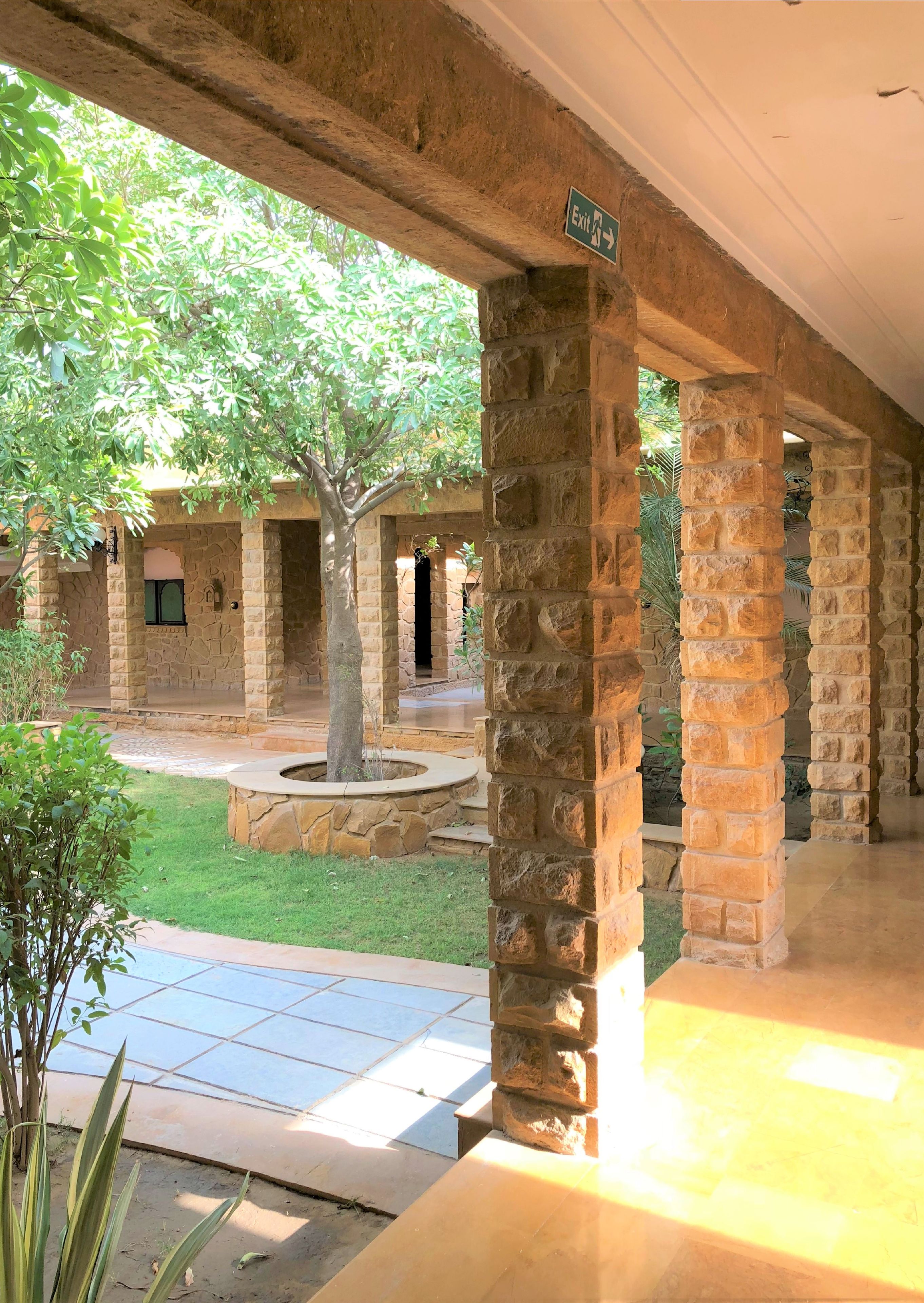 A stone courtyard with a covered walkway, a tree, and a sign indicating an exit.