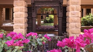 Un arco de piedra con un banco en su interior, rodeado de flores de buganvilla.
